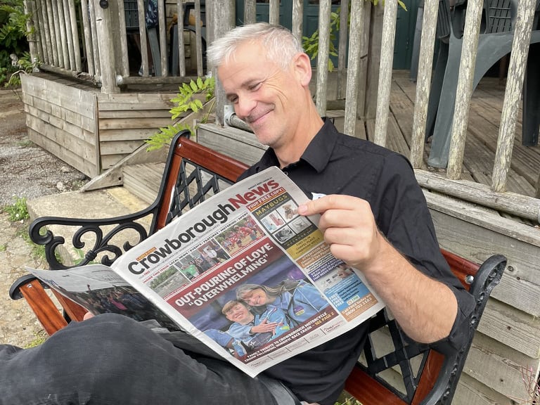 Simon sitting on a bench reading The Crowborough News.