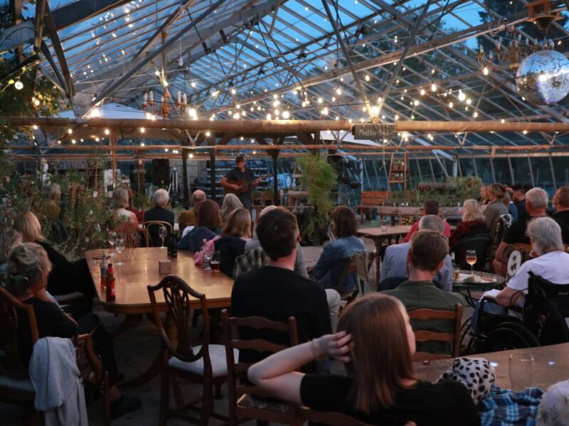 The audience in the greenhouse watching Tom Cole play his guitar