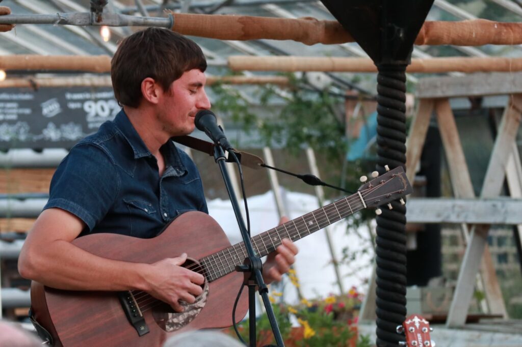 Tom Cole singing and playing the guitar in the greehouse.