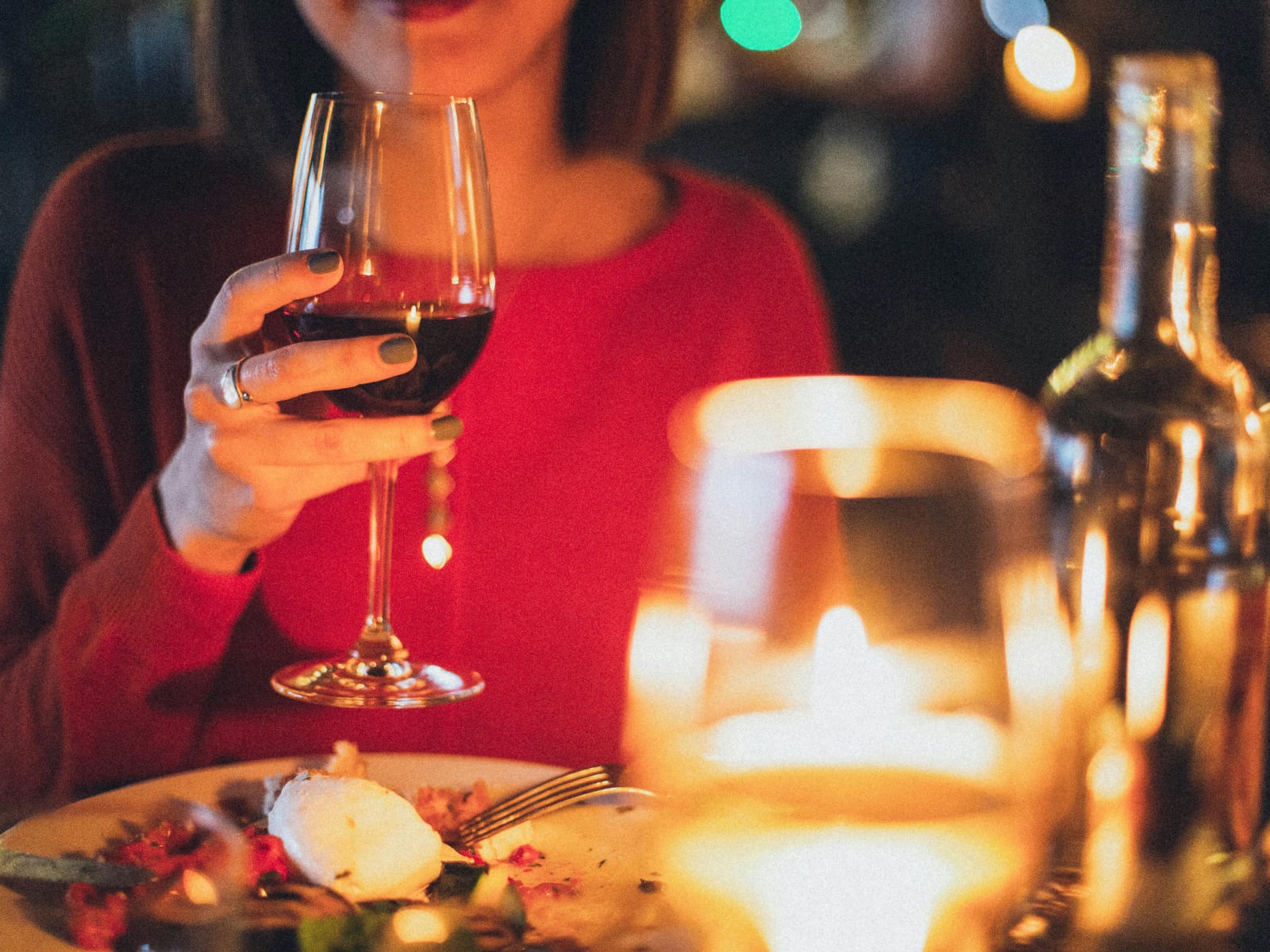 A candlelight dinner table with a woman holding a glass of red wine.