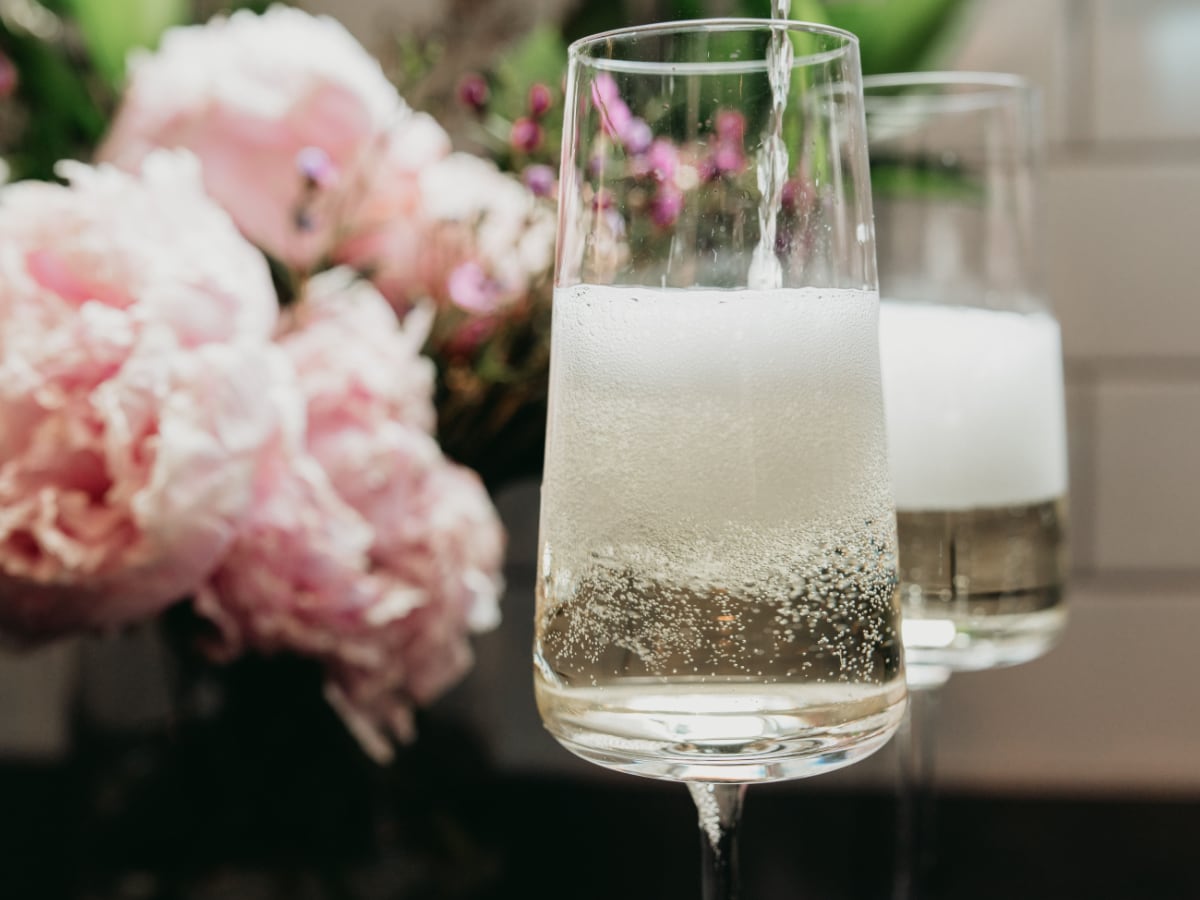 Two glasses of sparkling wine with pink peony flowers in the background.