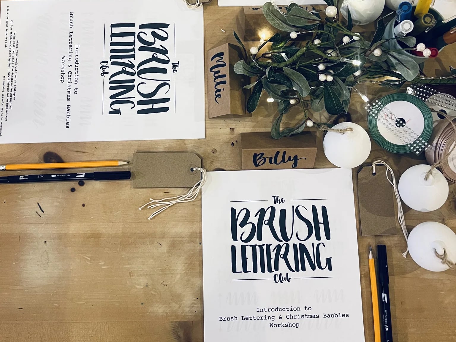 A table with Brush lettering workshop leaflets and Christmas baubles on.